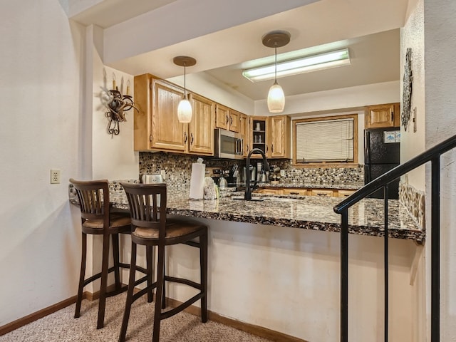 kitchen with stainless steel microwave, backsplash, a sink, dark stone countertops, and black fridge