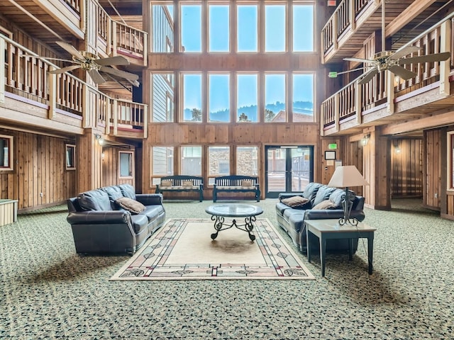 carpeted living area featuring a ceiling fan, plenty of natural light, and wooden walls