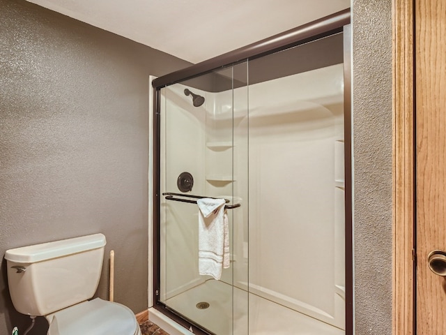 bathroom with toilet, a shower stall, and a textured wall