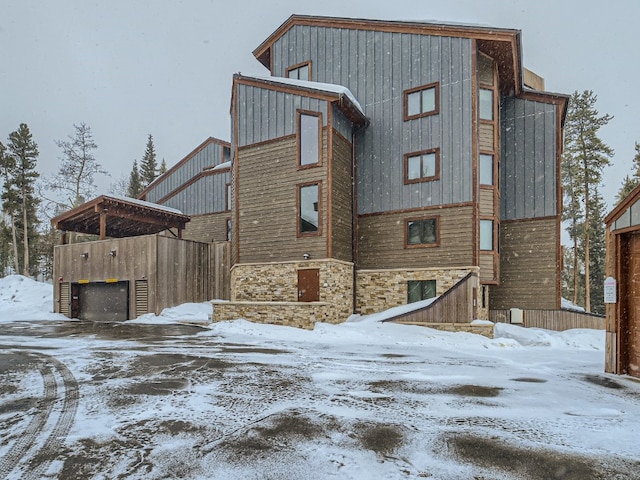 snow covered rear of property featuring a garage and stone siding