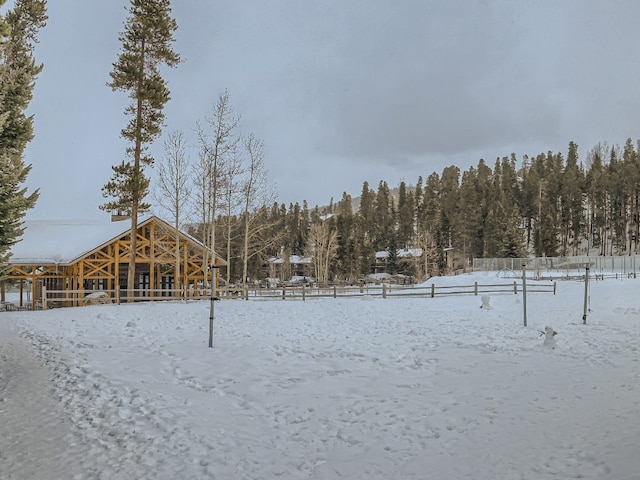 snowy yard with a forest view and fence