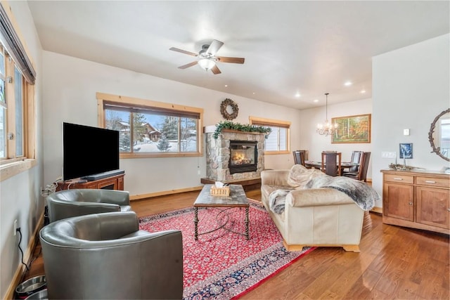 living room with baseboards, recessed lighting, ceiling fan with notable chandelier, a fireplace, and wood finished floors