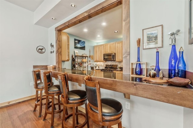 kitchen with light brown cabinets, light wood finished floors, a peninsula, stainless steel appliances, and tasteful backsplash