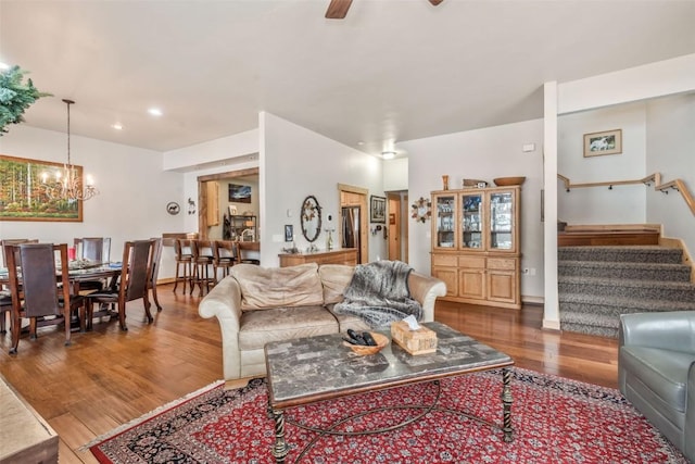 living area featuring wood finished floors, stairs, and ceiling fan with notable chandelier