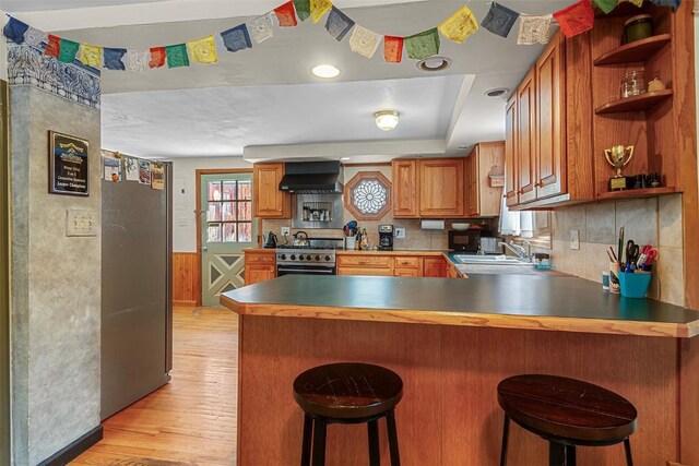 kitchen with a kitchen breakfast bar, light wood-type flooring, custom range hood, appliances with stainless steel finishes, and kitchen peninsula