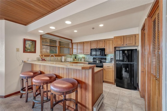 kitchen with black appliances, a baseboard heating unit, a kitchen breakfast bar, a peninsula, and light countertops