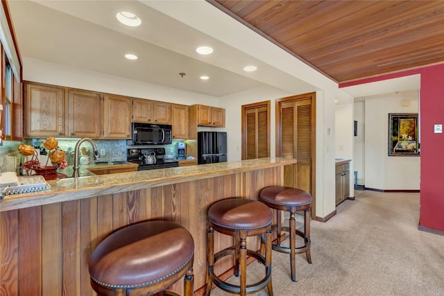 kitchen featuring tasteful backsplash, a breakfast bar, recessed lighting, a peninsula, and black appliances