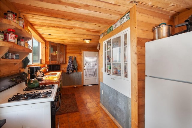 kitchen with white appliances, wooden walls, wooden ceiling, and sink