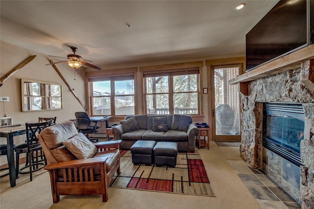 living room featuring a stone fireplace, ceiling fan, and light colored carpet