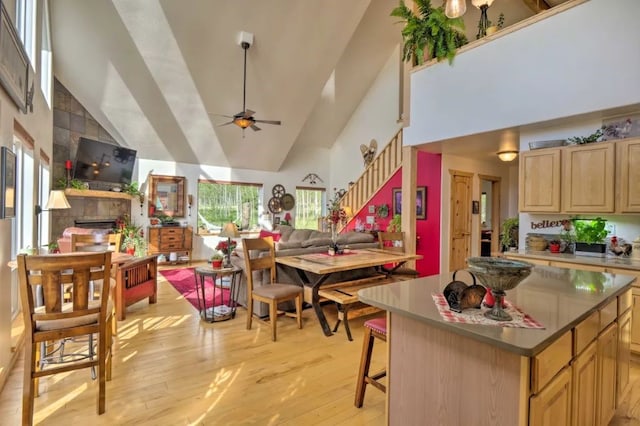 kitchen featuring ceiling fan, high vaulted ceiling, a center island, light hardwood / wood-style floors, and a breakfast bar area