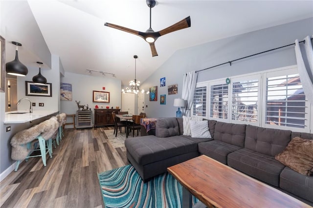 living room with ceiling fan with notable chandelier, hardwood / wood-style floors, lofted ceiling, sink, and track lighting