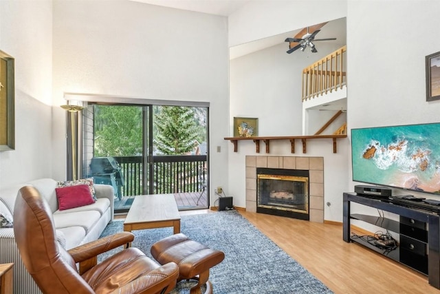 living room featuring ceiling fan, light hardwood / wood-style floors, a towering ceiling, and a fireplace