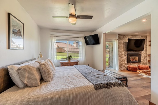 bedroom with a fireplace, light wood-type flooring, and ceiling fan