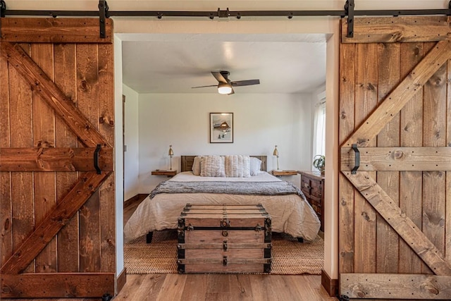 bedroom featuring a barn door, ceiling fan, and light wood-type flooring