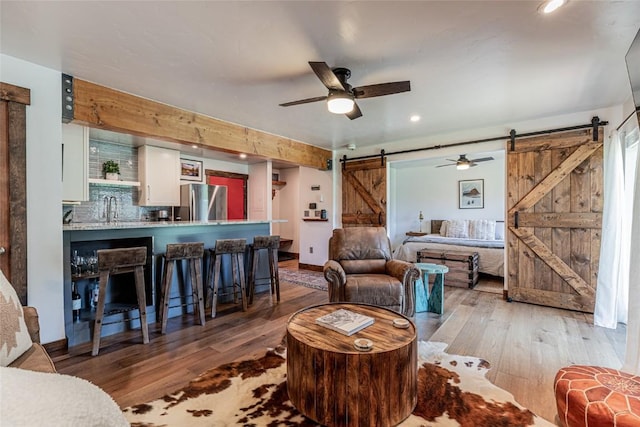 living room featuring a barn door, ceiling fan, light hardwood / wood-style flooring, and sink