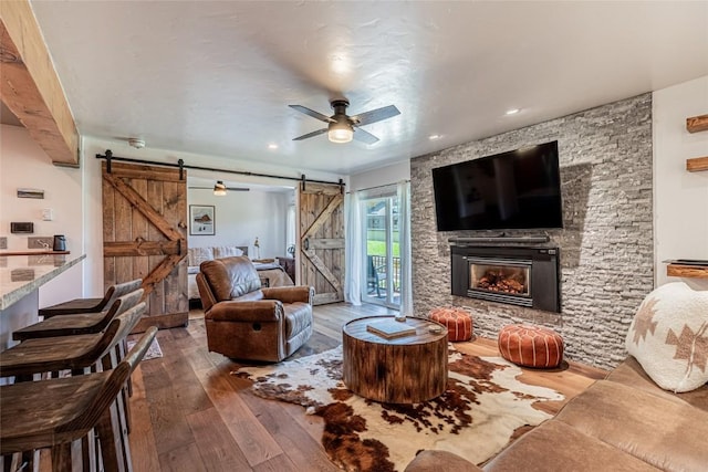 living room with a barn door, hardwood / wood-style flooring, a stone fireplace, and ceiling fan