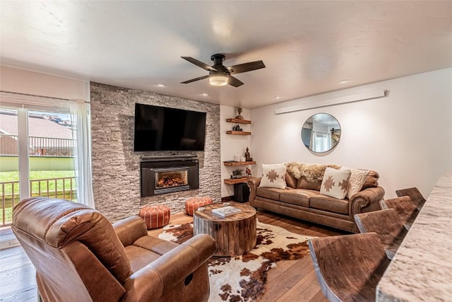 living room featuring light hardwood / wood-style flooring, a stone fireplace, and ceiling fan