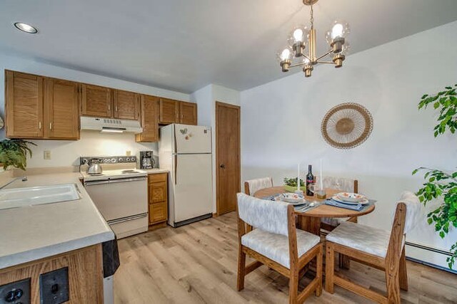 kitchen featuring white appliances, decorative light fixtures, light countertops, under cabinet range hood, and a sink