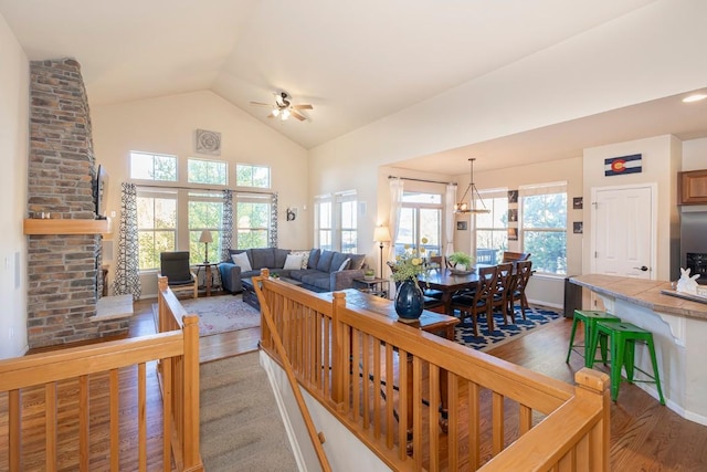 living room featuring wood-type flooring, ceiling fan with notable chandelier, a stone fireplace, and lofted ceiling