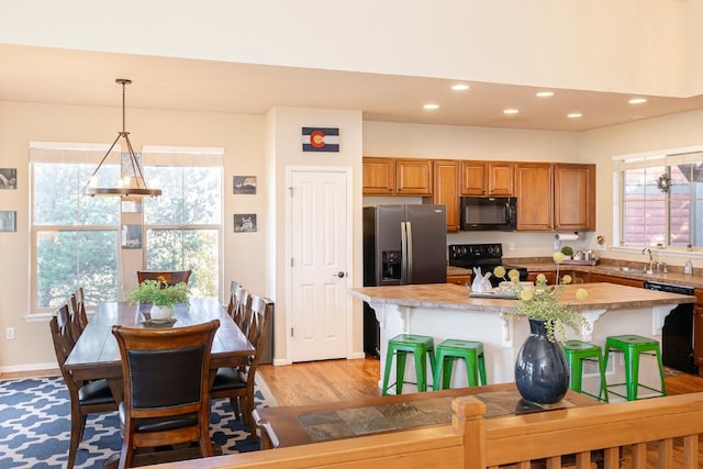 kitchen featuring a breakfast bar, black appliances, hanging light fixtures, light wood-type flooring, and a kitchen island