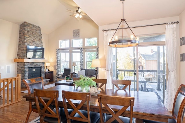 dining space featuring hardwood / wood-style flooring, ceiling fan with notable chandelier, a stone fireplace, and lofted ceiling