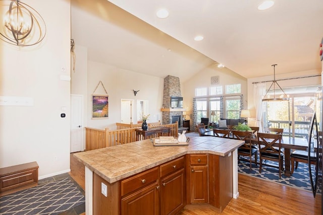 kitchen with wood-type flooring, a kitchen island, hanging light fixtures, and a stone fireplace