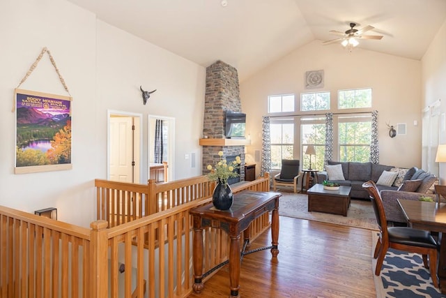 living room featuring ceiling fan, a stone fireplace, dark wood-type flooring, and high vaulted ceiling