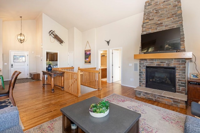 living room with a chandelier, hardwood / wood-style floors, high vaulted ceiling, and a fireplace