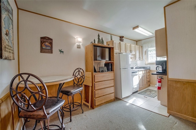 kitchen with sink, white refrigerator, stove, wooden walls, and light brown cabinetry