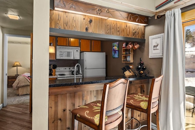 kitchen featuring white appliances, a breakfast bar, wood finished floors, and brown cabinetry