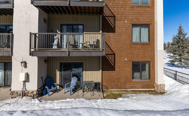 snow covered rear of property featuring a balcony and a patio