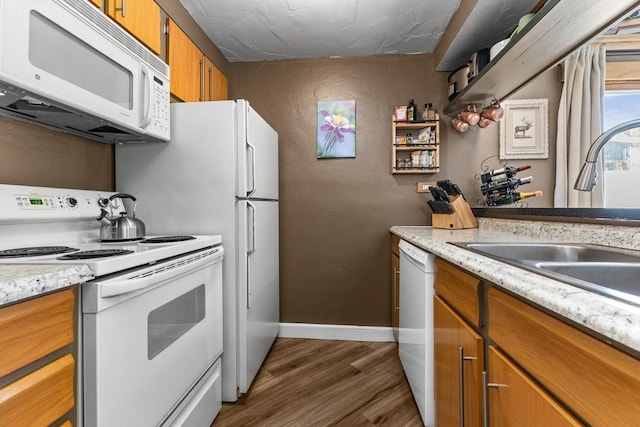 kitchen featuring a sink, dark wood-style floors, white appliances, brown cabinetry, and baseboards