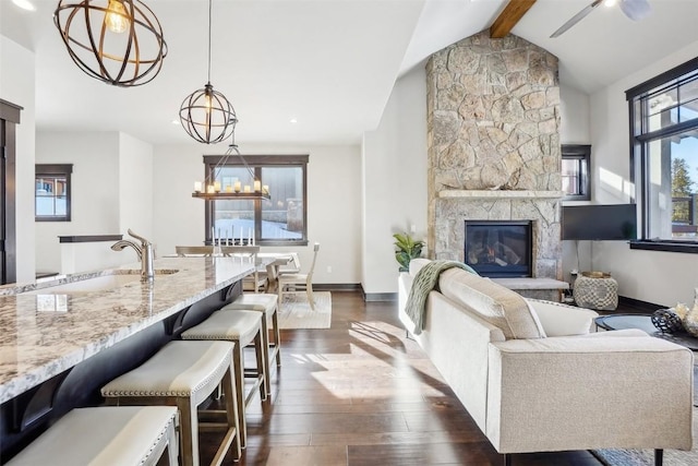 living room featuring ceiling fan, sink, a fireplace, vaulted ceiling with beams, and dark hardwood / wood-style floors