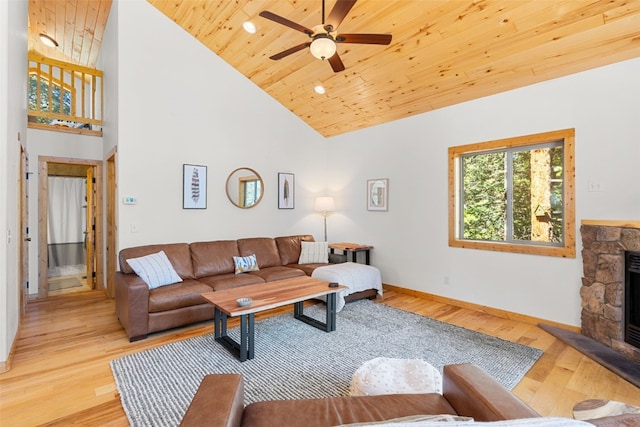 living room with ceiling fan, wooden ceiling, a stone fireplace, high vaulted ceiling, and light wood-type flooring