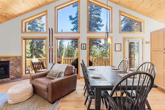 dining space featuring light wood-type flooring, high vaulted ceiling, and a stone fireplace