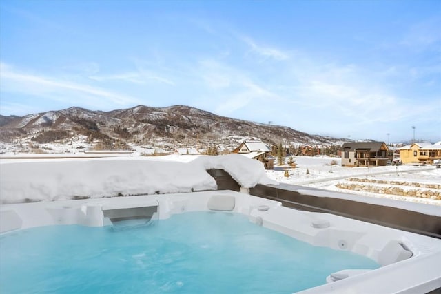 snow covered pool with a hot tub and a mountain view