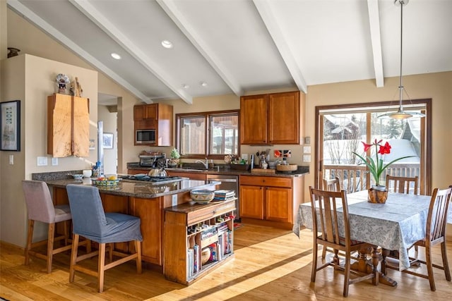 kitchen featuring sink, vaulted ceiling with beams, pendant lighting, stainless steel appliances, and light hardwood / wood-style floors