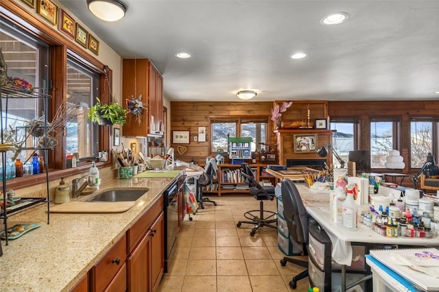 kitchen with sink, light stone counters, light tile patterned floors, wooden walls, and dishwasher