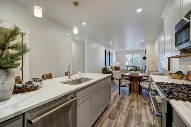 kitchen with sink, decorative light fixtures, appliances with stainless steel finishes, dark hardwood / wood-style flooring, and light stone countertops