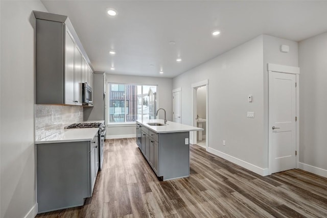 kitchen with gray cabinets, appliances with stainless steel finishes, sink, dark hardwood / wood-style flooring, and a center island with sink