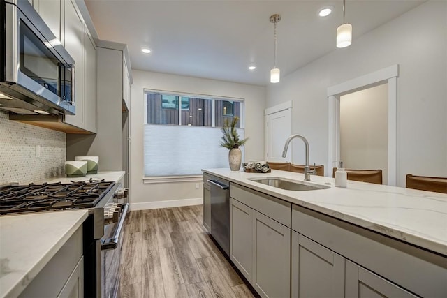 kitchen with sink, gray cabinetry, pendant lighting, stainless steel appliances, and light stone countertops