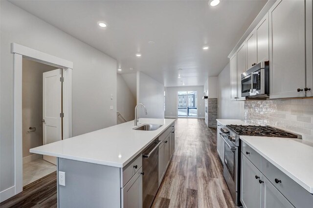 kitchen featuring sink, backsplash, stainless steel appliances, an island with sink, and light wood-type flooring