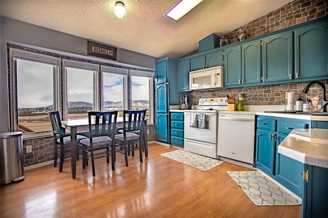 kitchen with a sink, white appliances, light wood-style floors, light countertops, and vaulted ceiling