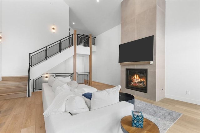 living room with a fireplace, a towering ceiling, and light wood-type flooring