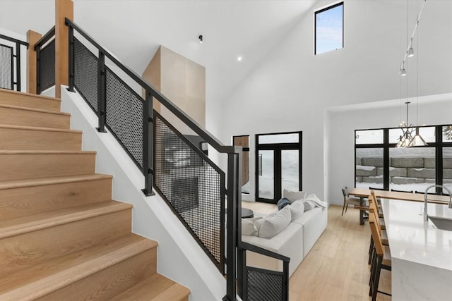 staircase with a chandelier, a high ceiling, hardwood / wood-style flooring, and a healthy amount of sunlight