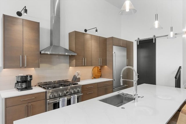 kitchen featuring pendant lighting, high quality appliances, wall chimney range hood, a barn door, and tasteful backsplash