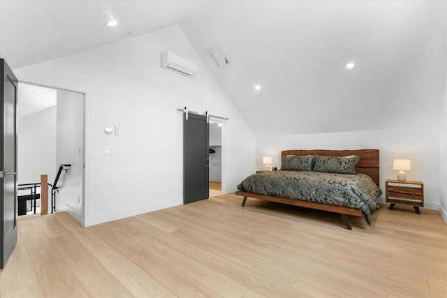 bedroom with a barn door, lofted ceiling, a wall mounted air conditioner, and light wood-type flooring