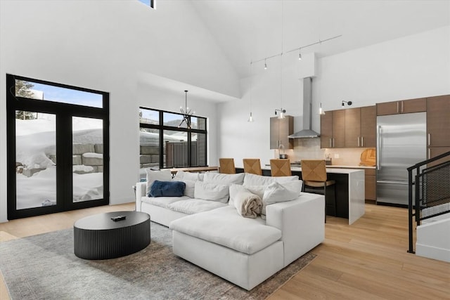 living room with a notable chandelier, a healthy amount of sunlight, high vaulted ceiling, and light hardwood / wood-style flooring