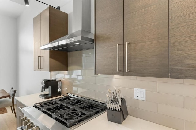 kitchen featuring stove, wall chimney range hood, light hardwood / wood-style flooring, tasteful backsplash, and cooktop