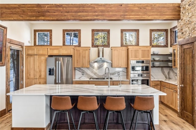 kitchen with appliances with stainless steel finishes, backsplash, wall chimney exhaust hood, a spacious island, and beam ceiling